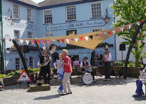 Outdoor scene with a band playing music and people dancing near a blue building.